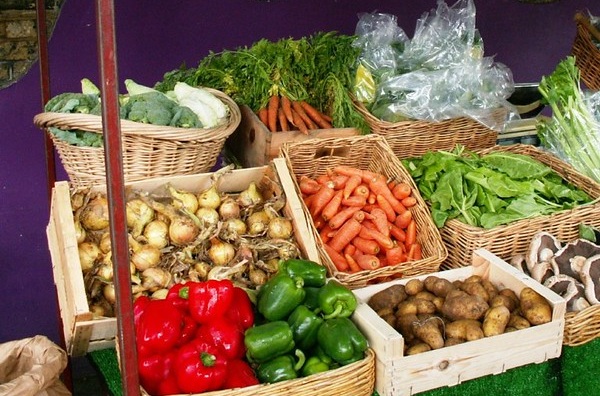 Onions, carrots, peppers, potatoes and mushrooms displayed in crates and baskets on a market stall