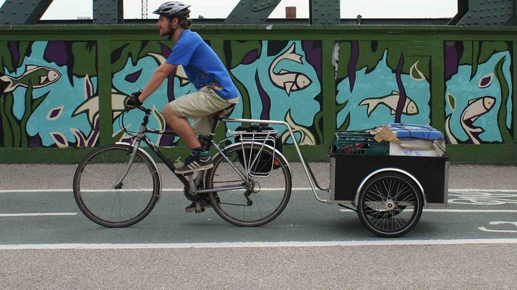 OrganicLea delivery person riding a bicycle attached to a trailer full of box scheme veg bags