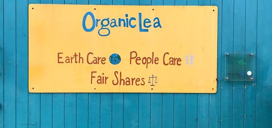 Signage on the blue-painted entrance to an OrganicLea building with the words OreganicLea - Earth Care - People Care - Fair Shares